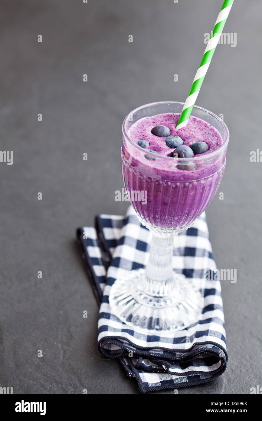 Nahaufnahme der Heidelbeer-Milch-Smoothie in Glas mit gestreiften Stroh auf karierte Serviette auf dunklem Hintergrund Stockfoto