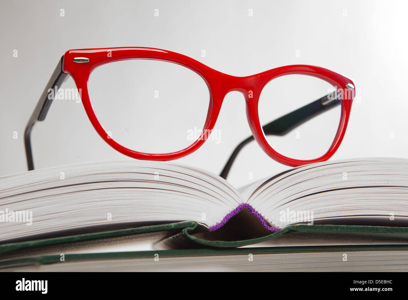 rote Brille auf offenes Buch über weiß Stockfoto