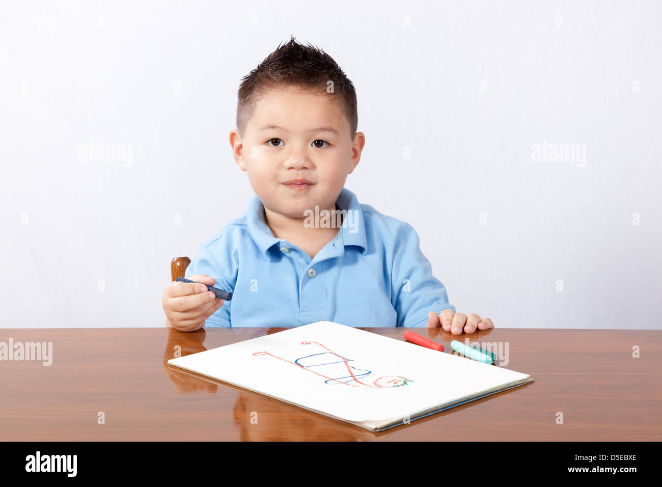 süße junge sitzt an einem Holztisch mit Papier und Bleistift, schreiben und zeichnen auf dem Papier Stockfoto