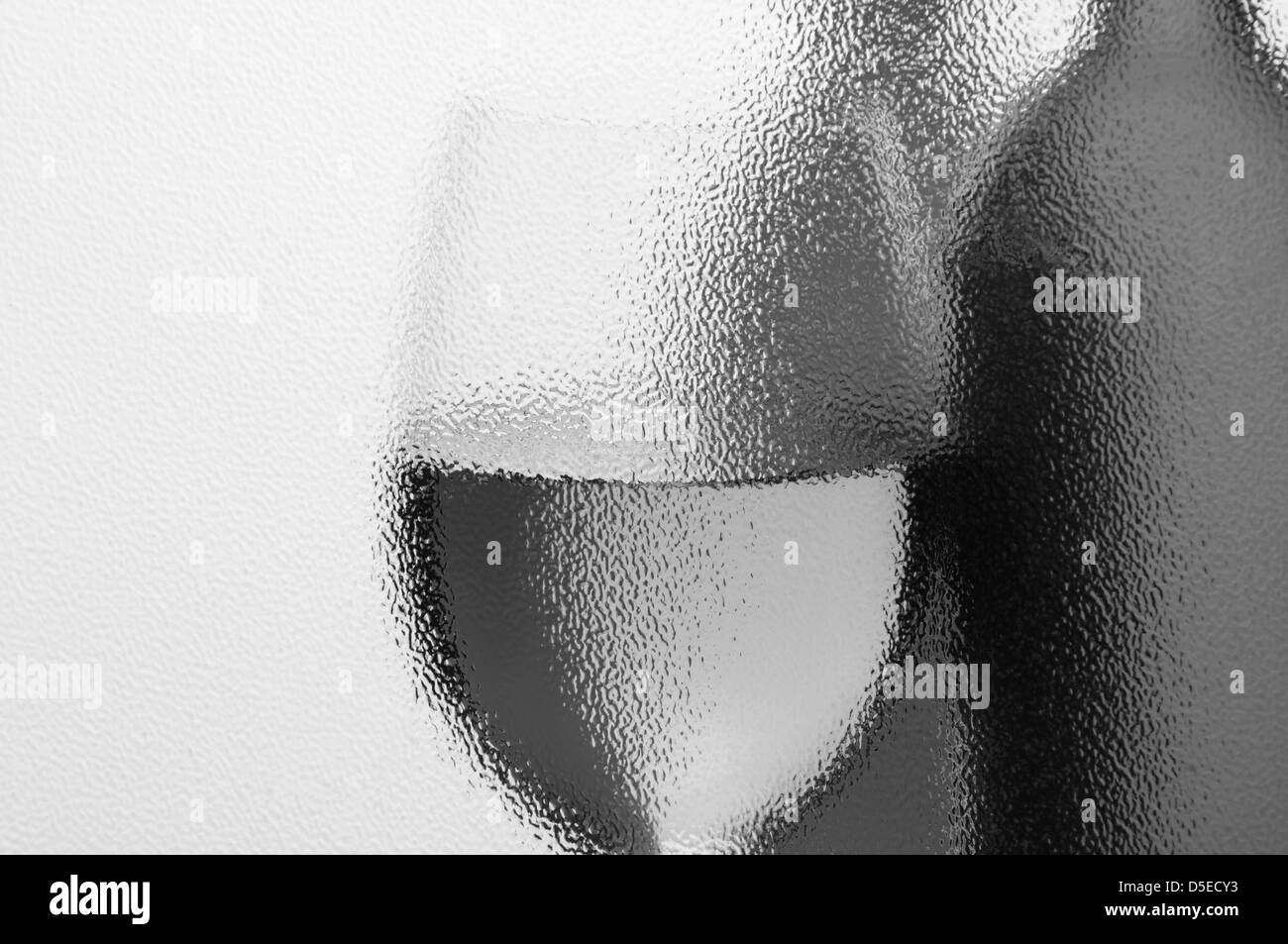 Wein-Flaschen und Weinglas in Monotone durch ein strukturiertes Fenster mit Hintergrundbeleuchtung zu sehen. Horizontale Komposition mit Exemplar. Stockfoto