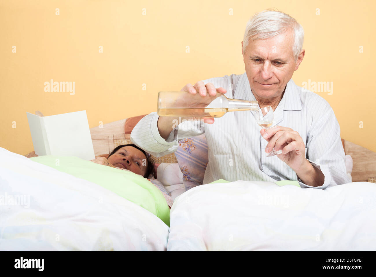 Senior mit Flasche Alkohol und Frau Mann ältere Menschen mit Buch im Bett Stockfoto