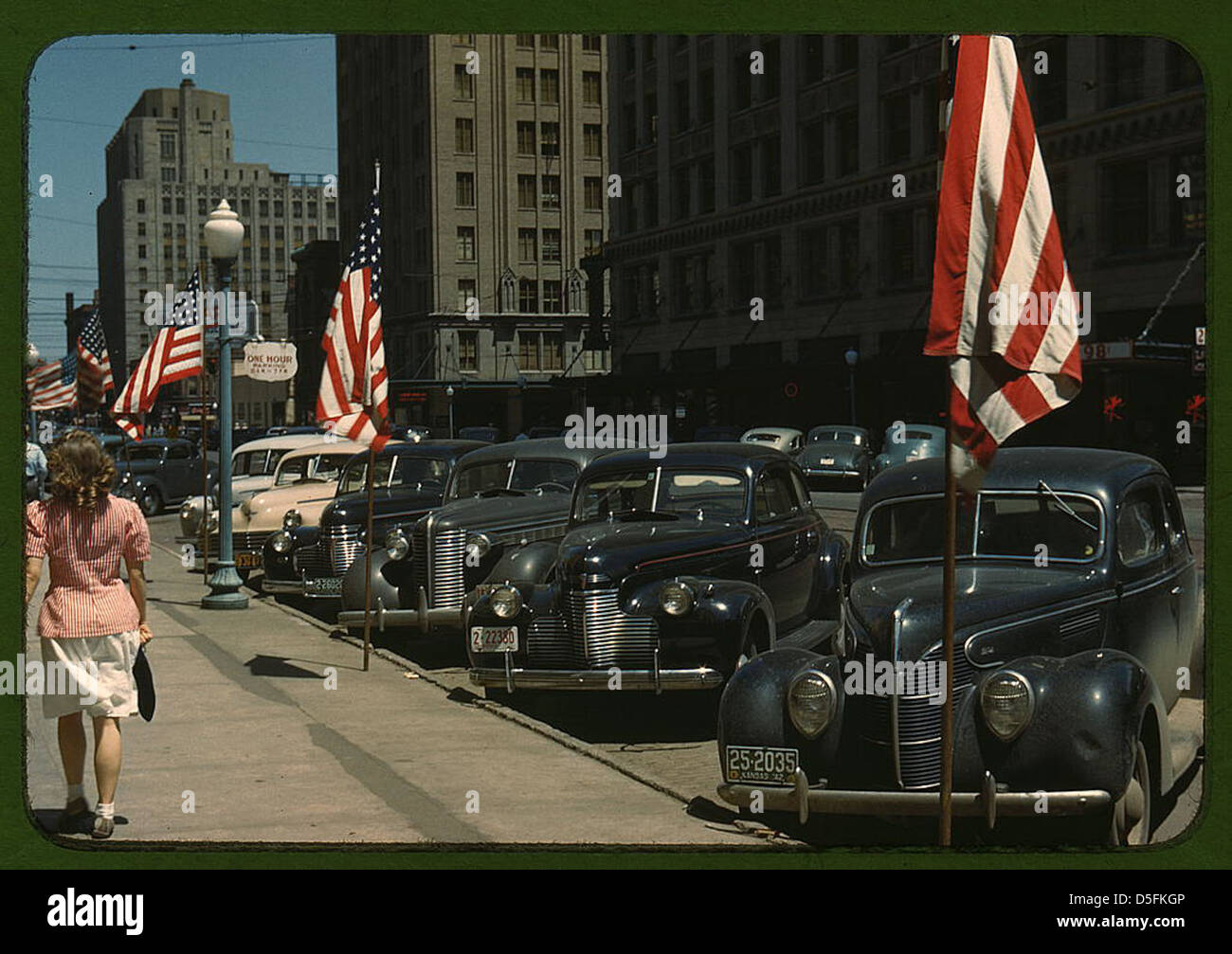 Ein Foto von Lincoln, Nebraska aus dem Jahr 1942, das amerikanische Autos, Stadtflaggen und Fußgänger zeigt, die durch die Straßen laufen. Das Bild bietet eine Momentaufnahme des amerikanischen Stadtlebens Mitte des 20. Jahrhunderts. Stockfoto