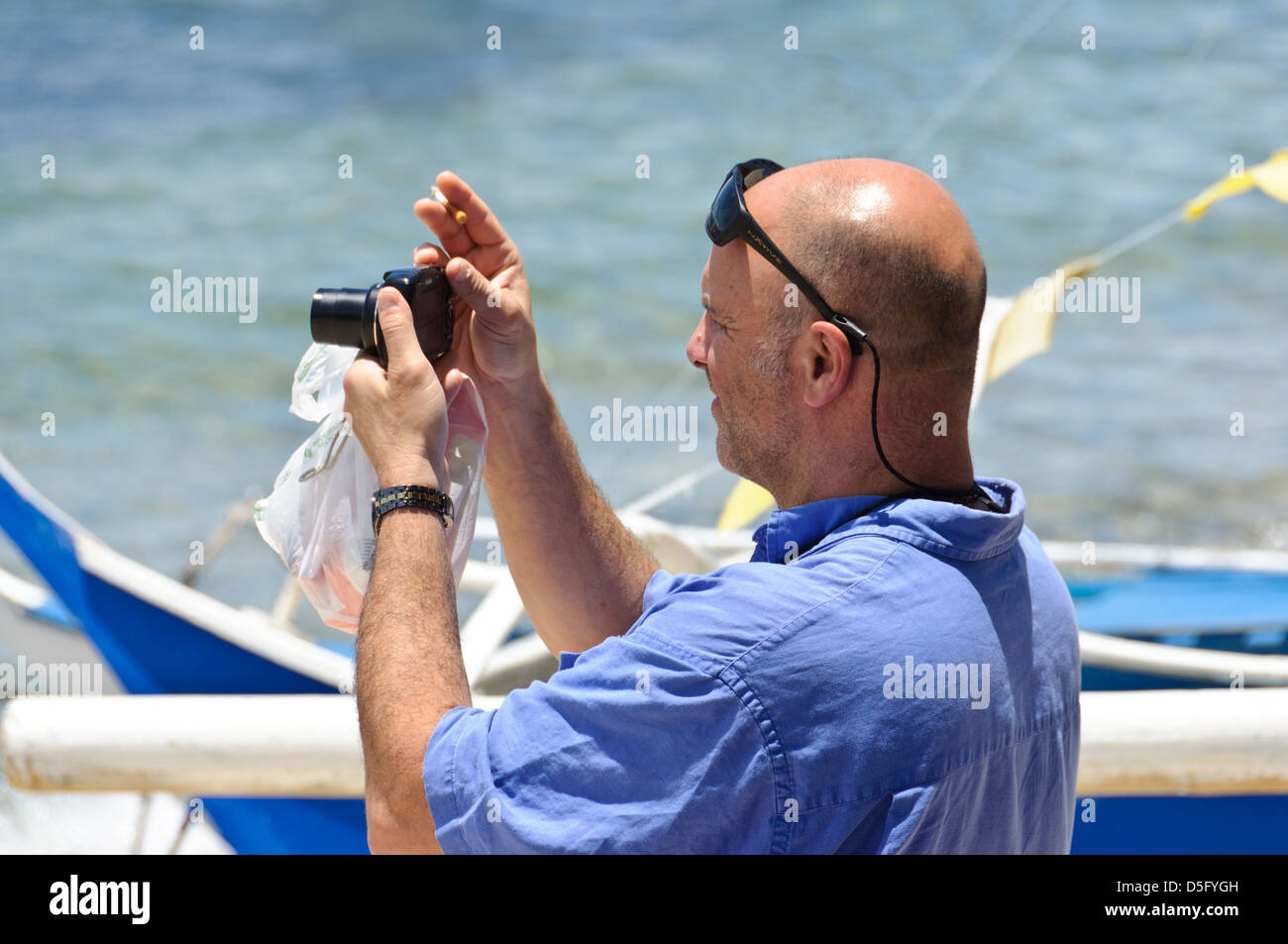 Kaukasischer Mann mittleren Alters mit Glatze und Sonnenbrille auf der Stirn nimmt Urlaub Bilder mit einer Canon Punkt & shoot-Kamera - Sabang, Philippinen Stockfoto