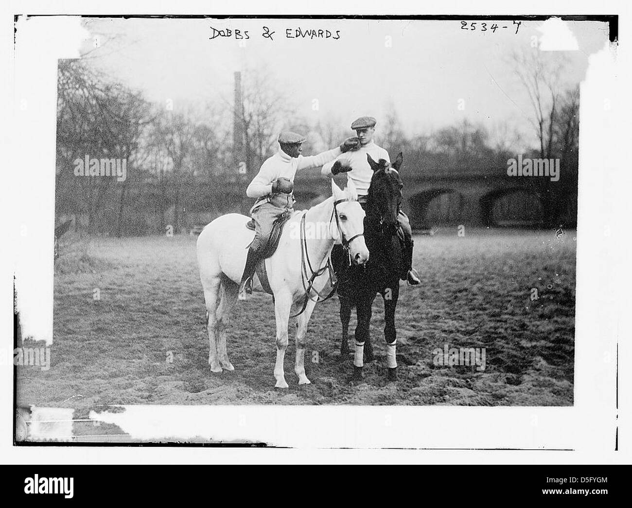 Dieses Schwarzweiß-Foto zeigt zwei Männer, Dobbs und Edwards, die mit einem Pferdegestüt in Verbindung gebracht wurden. Das Bild zeigt sie in lässiger Kleidung, einschließlich Rollkragen und Kappen, die möglicherweise ihre Arbeit oder ihren Lebensstil in der Pferdeindustrie repräsentieren. Stockfoto