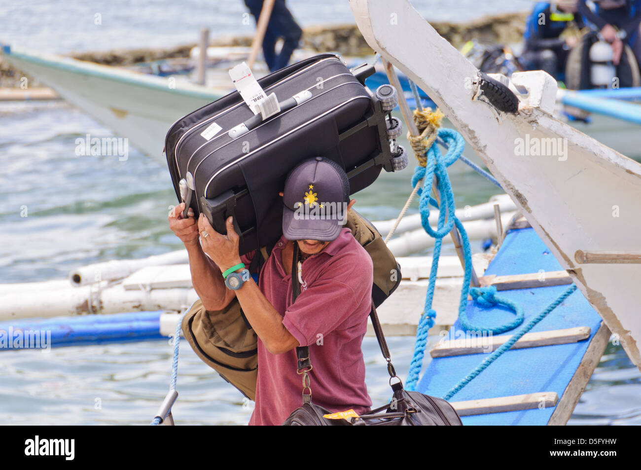 Männliche asiatische Portier trägt großes schweres Gepäck von einer kleinen Passagier-Fähre – Sabang, Puerto Galera, Philippinen, Asien Stockfoto