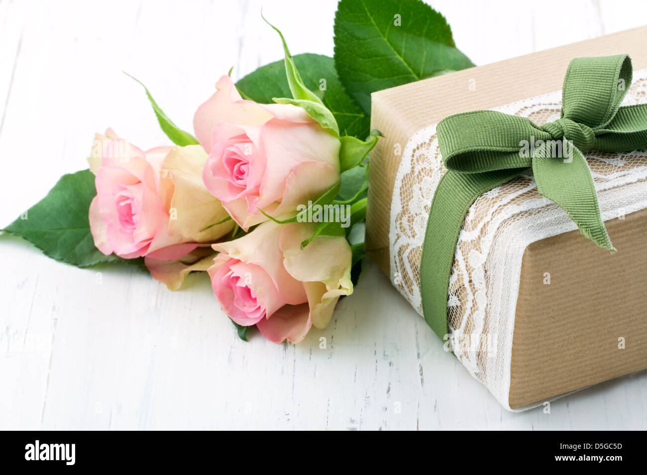 Geschenkbox verpackt in braunem Papier, weißer Spitze und einer grünen Schleife mit rosa Rosen auf Holz Vintage-Hintergrund Stockfoto