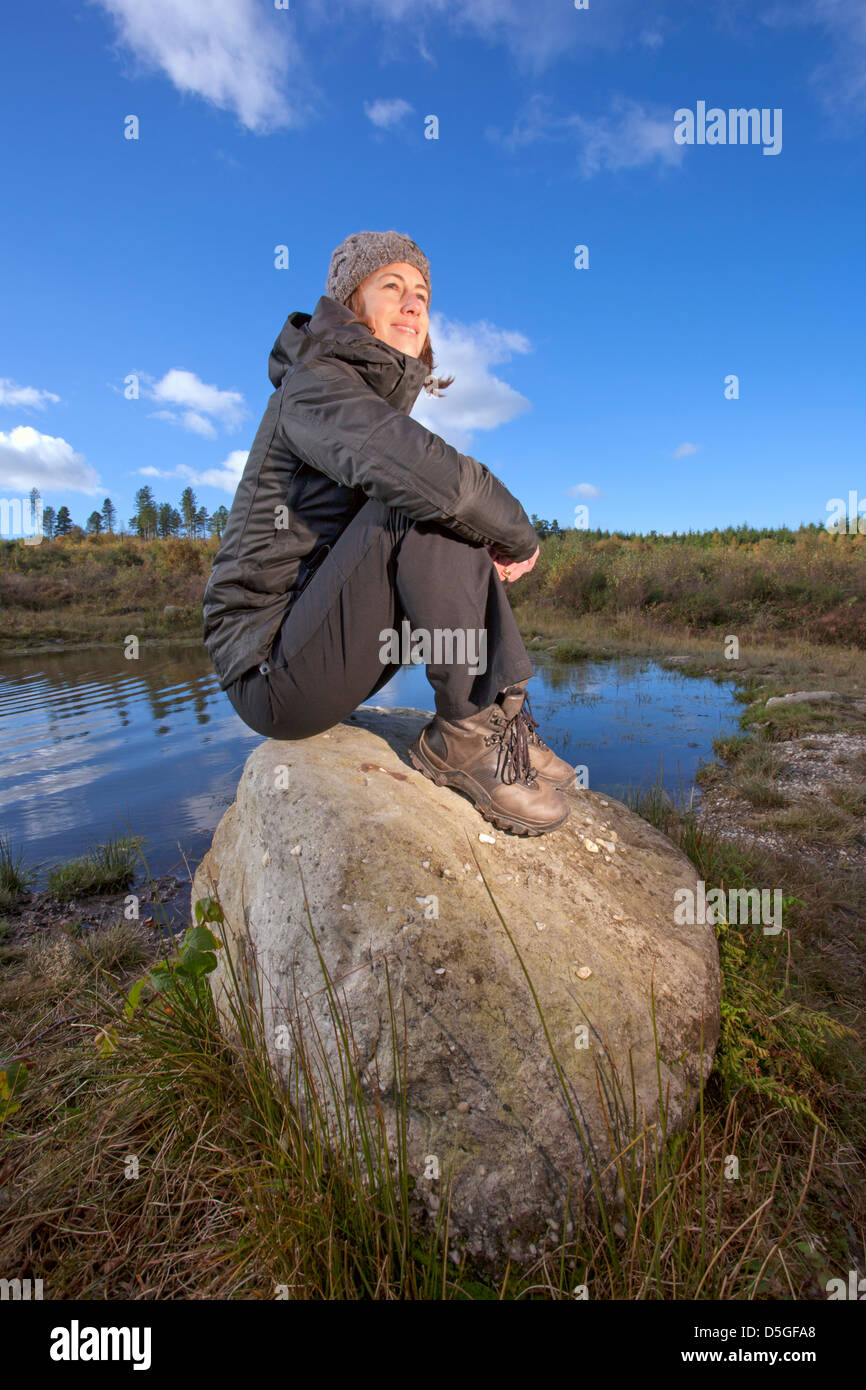 Junge Frau sitzt auf den Felsen in der Nähe von einem Teich. Stockfoto