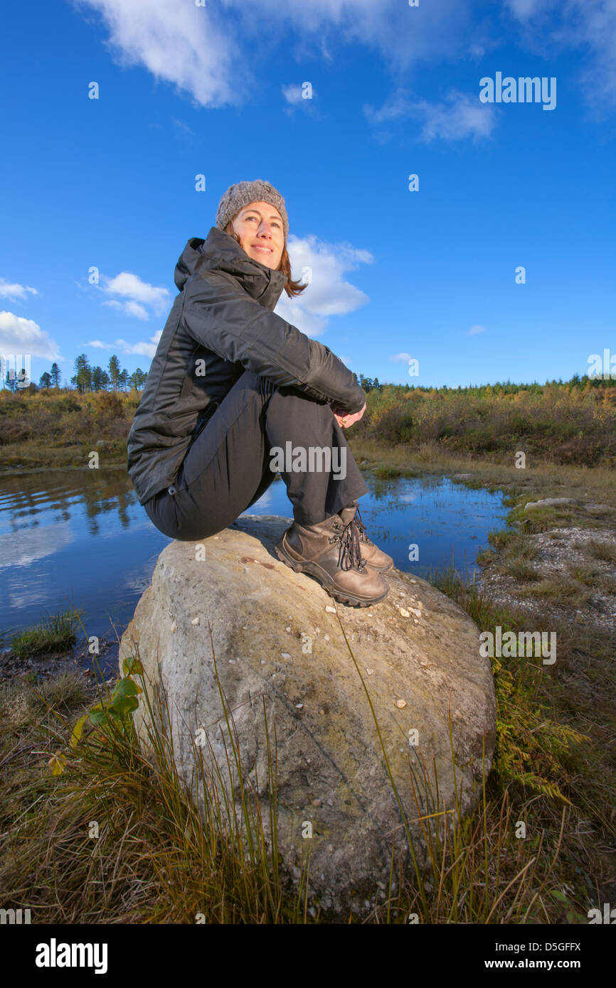 Junge Frau sitzt auf den Felsen in der Nähe von einem Teich. Stockfoto