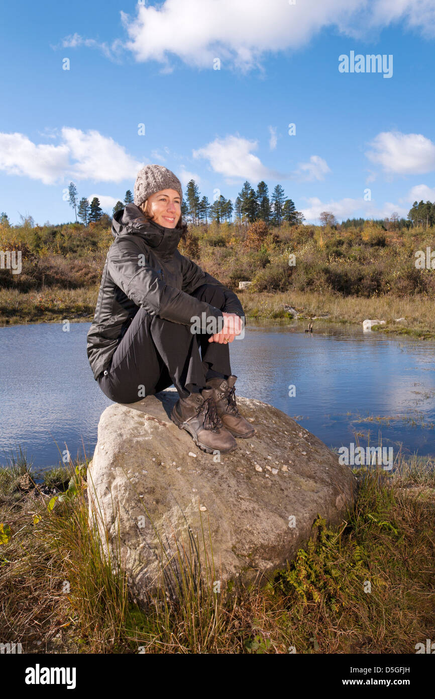 Junge Frau sitzt auf den Felsen in der Nähe von einem Teich. Stockfoto