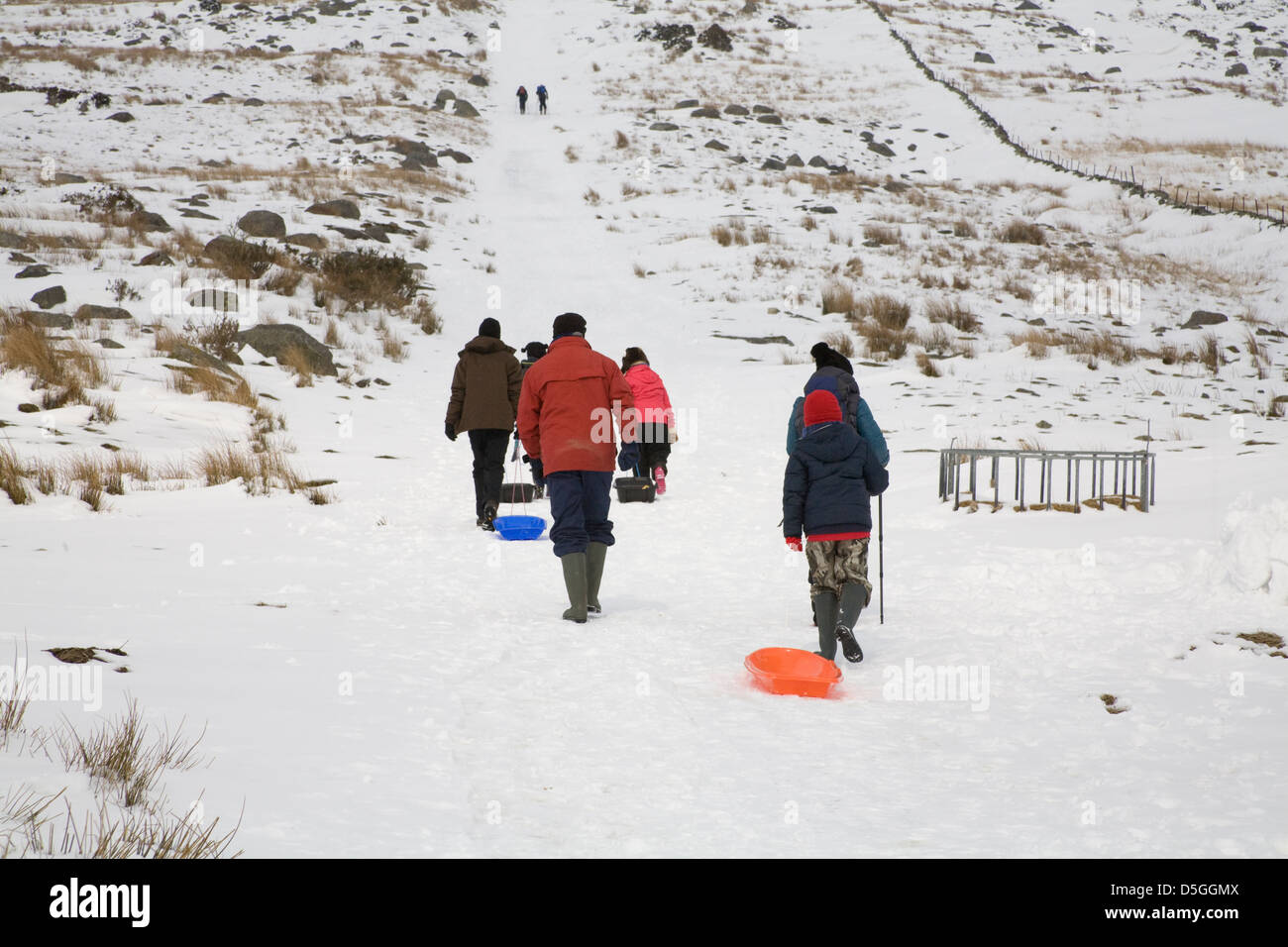 Conwy North Wales März Familiengruppe zu Fuß entlang einer Schnee bedeckten Strecke Kinder ziehen Schlitten Stockfoto
