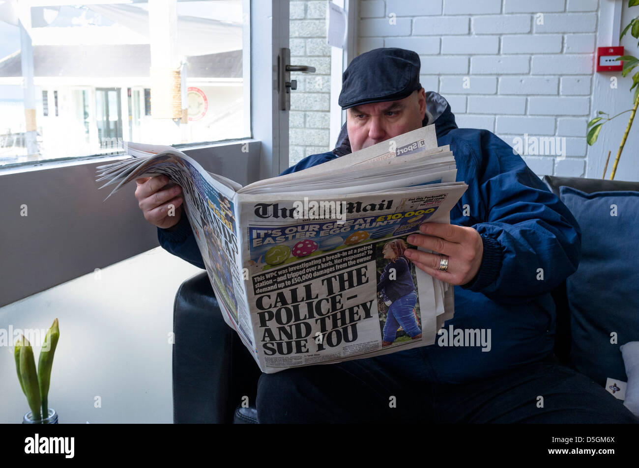 Ein Mann in eine flache Kappe liest der Daily Mail in einem Coffee-shop Stockfoto