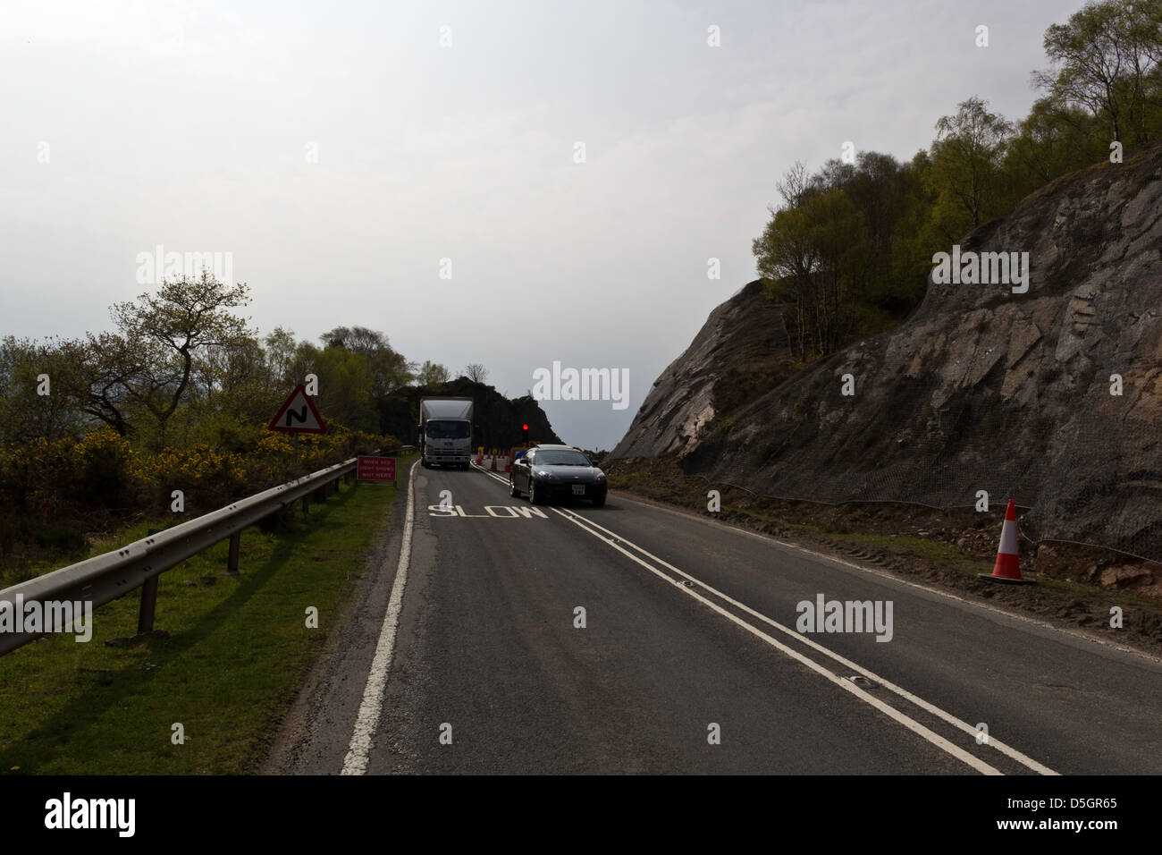 PKW- und LKW überqueren einer Straße zu reparieren Abschnitt der Autobahn in den schottischen Highlands. Die Straße verengt sich deutlich mit Stop-Schild Stockfoto