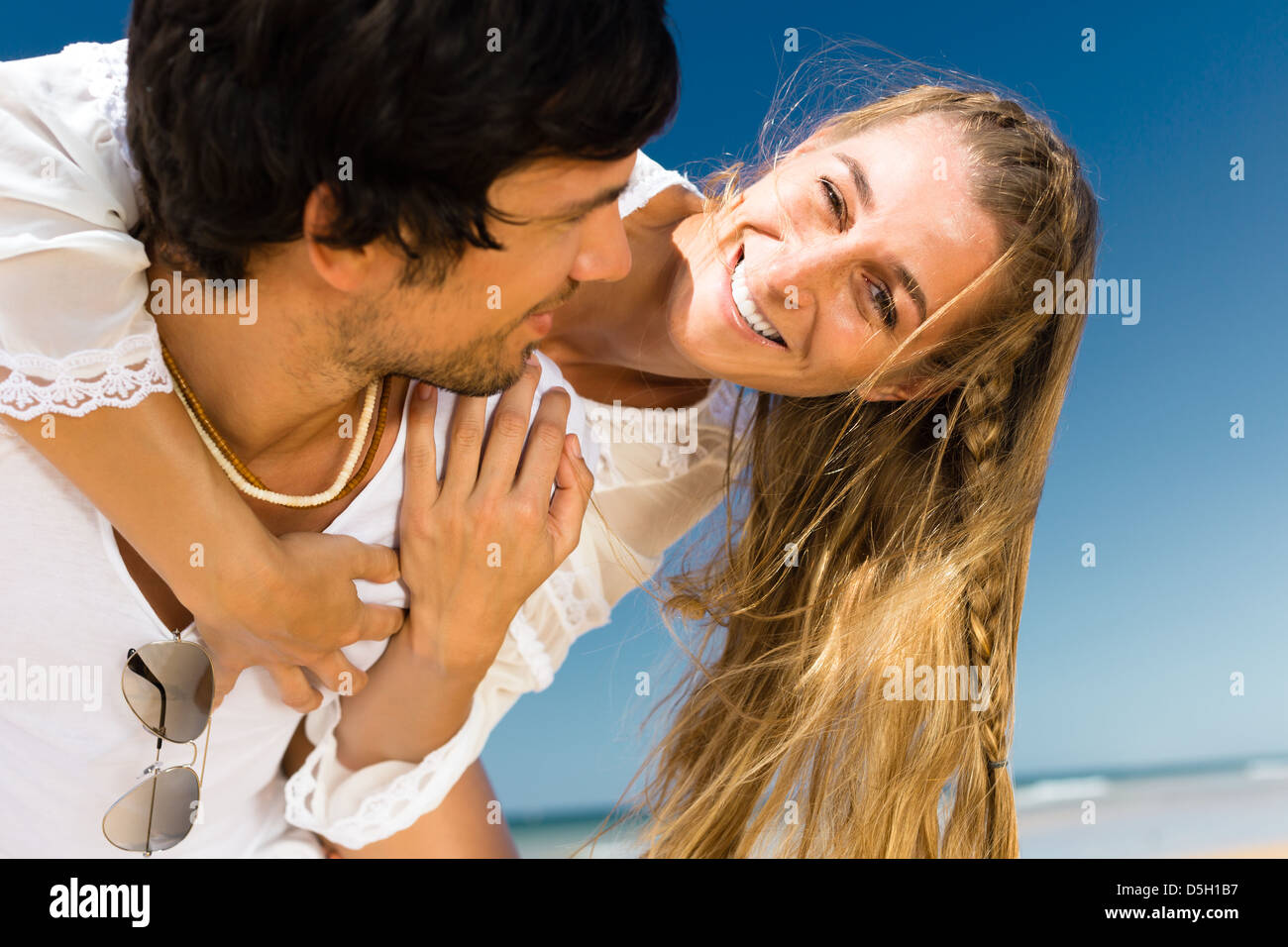 Verspieltes paar am Strand und Meer genießen ihren Sommerurlaub, trägt der Mann die Frau Huckepack Stockfoto