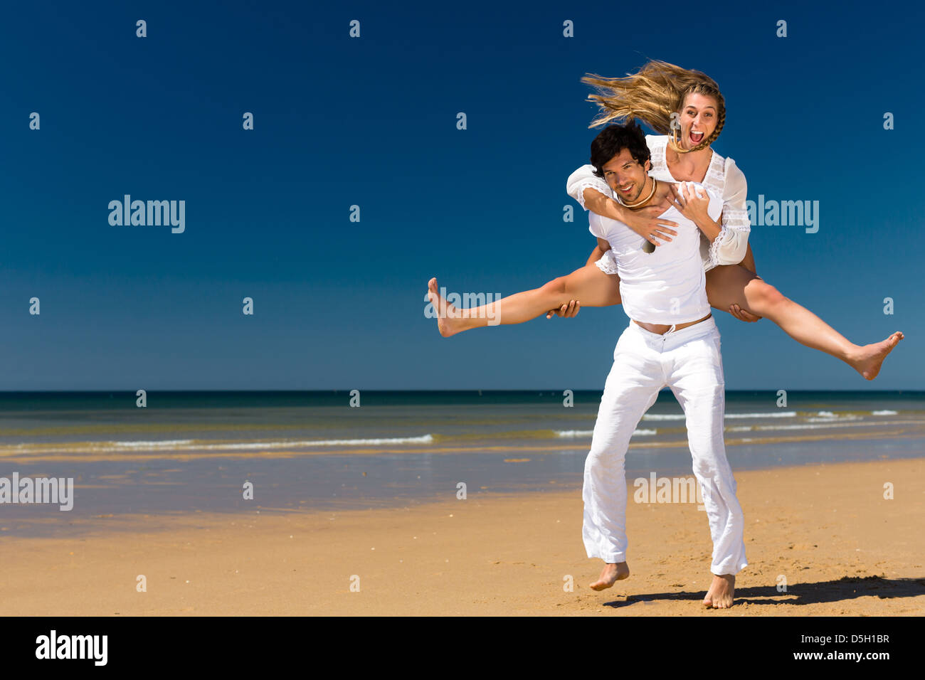 Verspieltes paar am Strand und Meer genießen ihren Sommerurlaub, trägt der Mann die Frau Huckepack Stockfoto