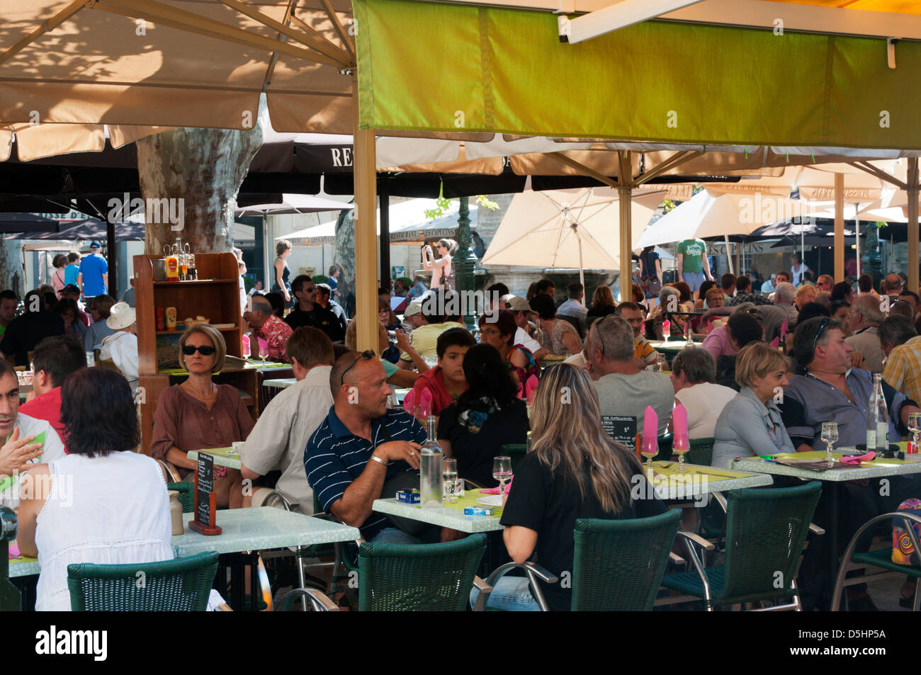 Touristen und Urlauber sitzen an Tischen im Freien ein Café in einem Stadtplatz in Südfrankreich. Stockfoto
