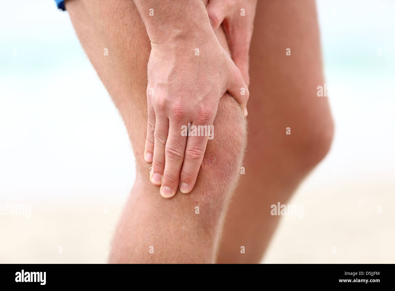 Nahaufnahme der männlichen Läufer mit Schmerzen in Kniegelenken am Strand Stockfoto