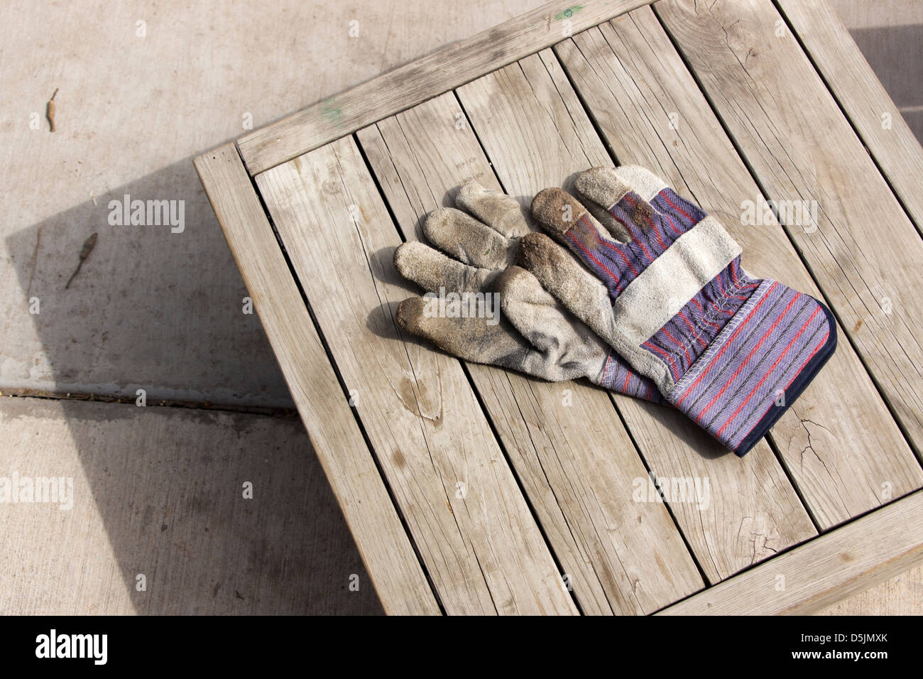 Schmutzige Arbeitshandschuhe auf einem verwitterten Holztisch liegend Stockfoto