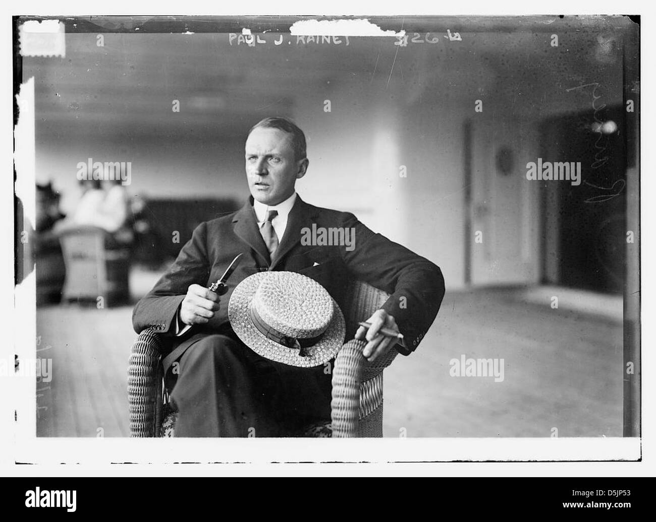 Ein Porträt von Paul J. Rainey, der in einem Korbstuhl sitzt und eine Zigarre raucht. Er trägt einen Strohhut, der eine wohlhabende Figur aus dem frühen 20. Jahrhundert darstellt. Stockfoto