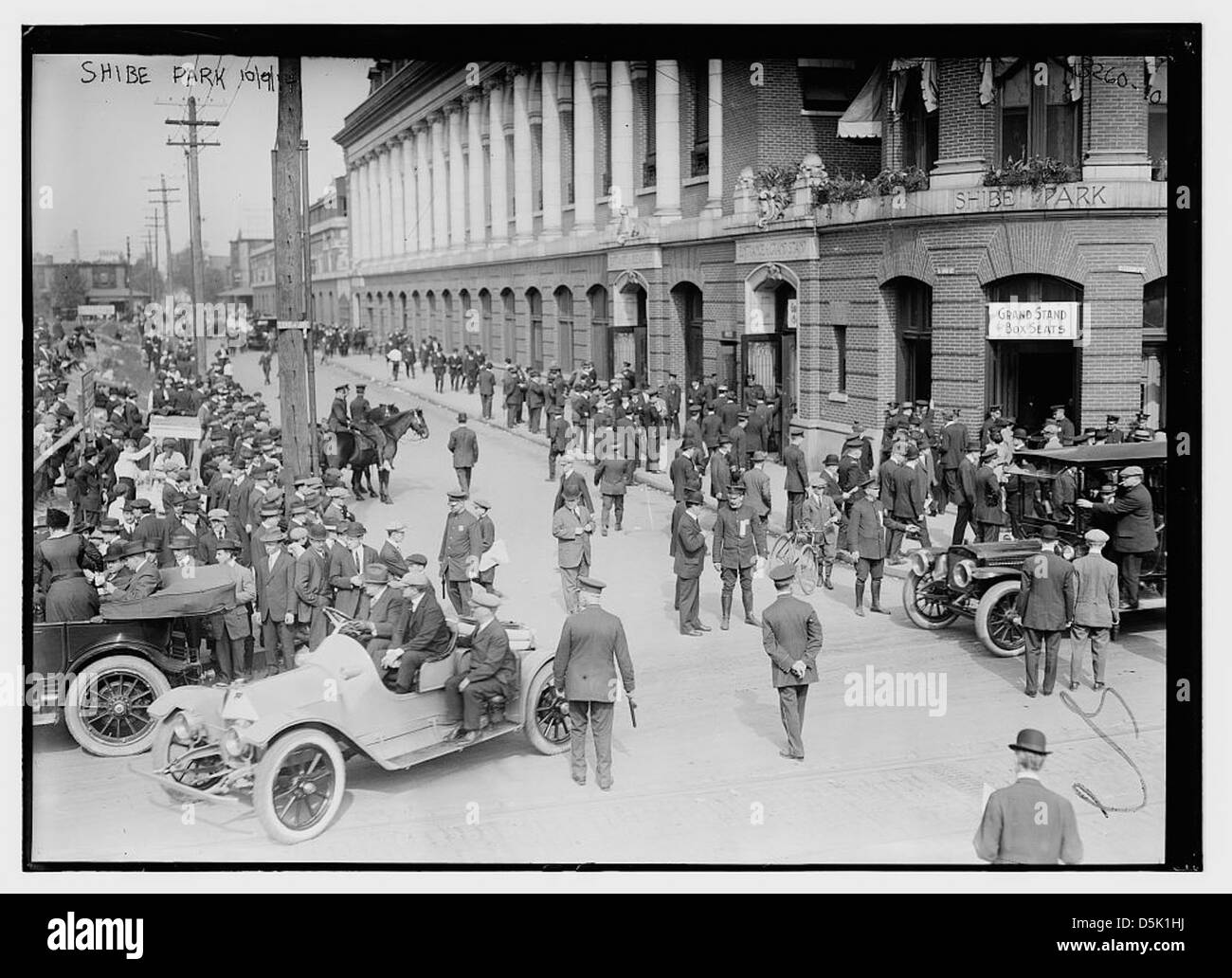 Dieses Foto zeigt die World Series 1914 im Shibe Park in Philadelphia mit Autos, berittenen Polizisten und Zuschauern. Das Bild fängt die lebhafte Atmosphäre der Veranstaltung mit Autos, Polizeibeamten und Pferdepatrouillen rund um das berühmte Baseballstadion ein. Stockfoto