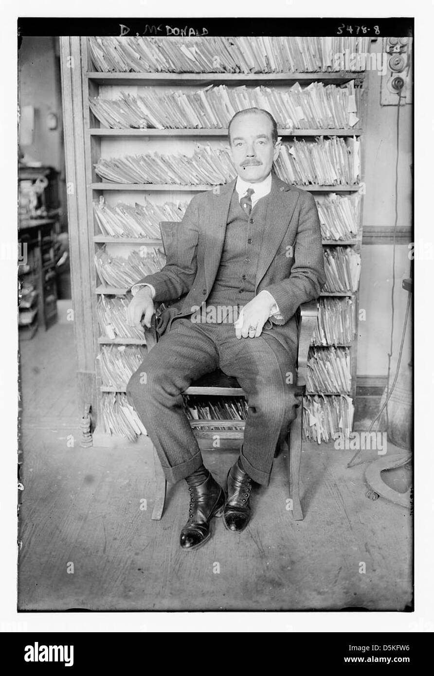 Dieses Porträt von D. McDonald zeigt einen Glatzen Mann mit Schnurrbart, der in einem Büro sitzt und Regale im Hintergrund sichtbar sind. Stockfoto