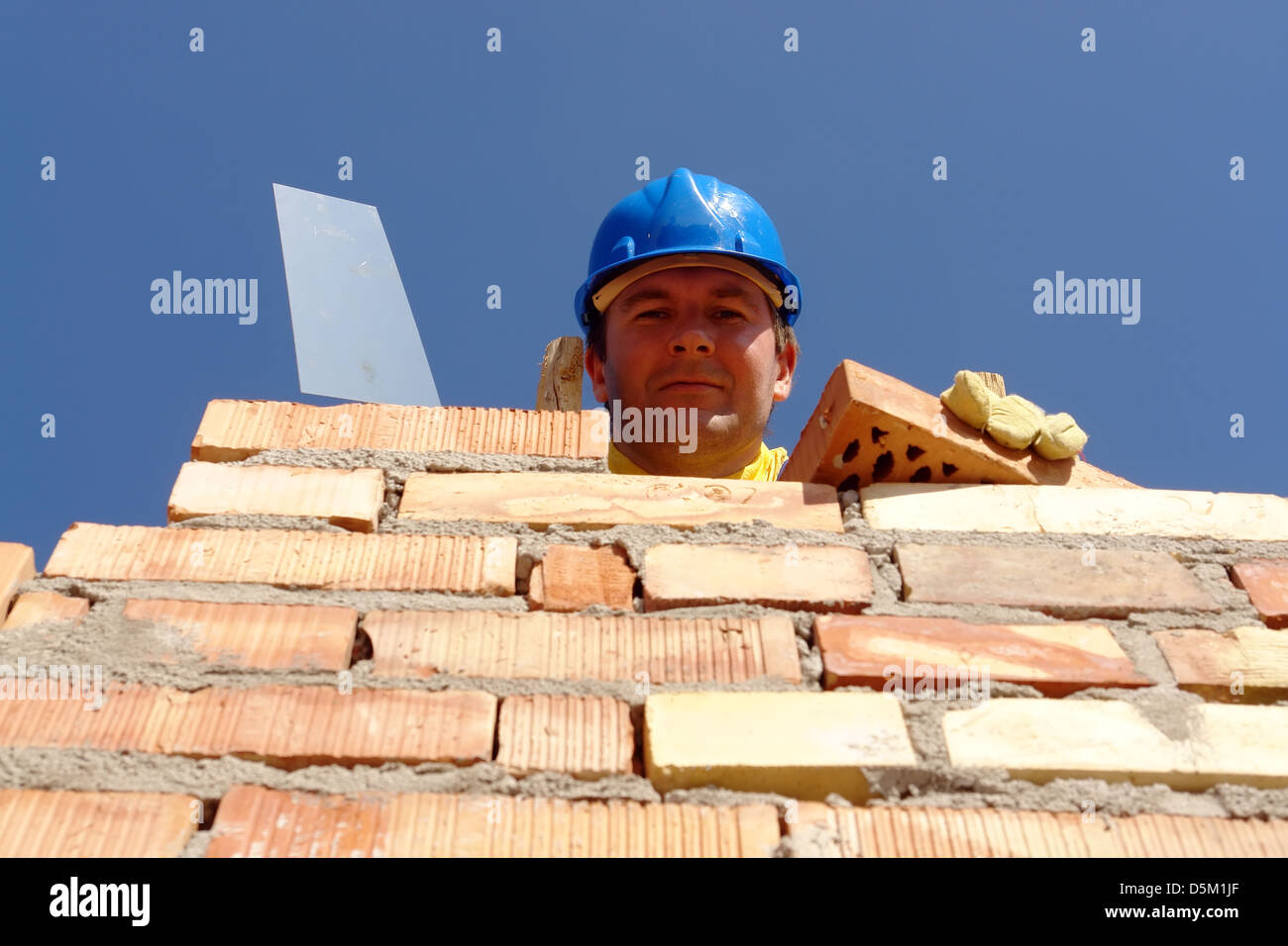 Bauarbeiter mit blauen Helm mit Edelstahl-Kelle und blickte von Mauer Ziegel Stockfoto