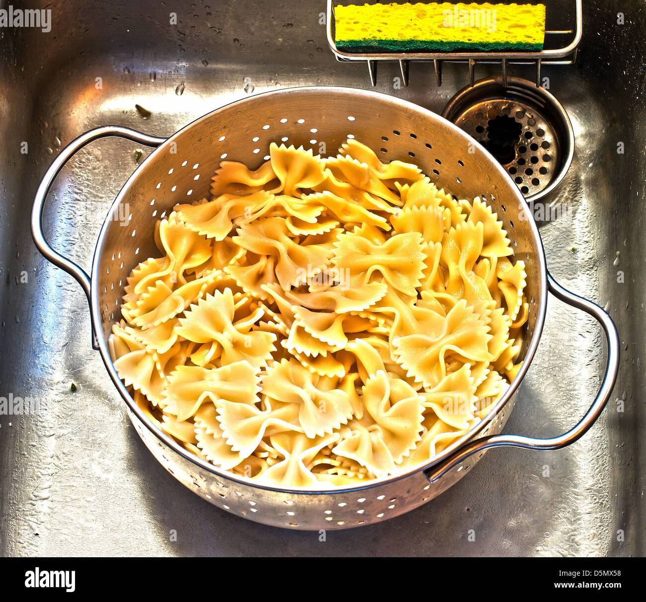 Frisch gekochtes Farfalle oder Fliege, Nudeln in Sieb in der Spüle mit hellen gelben Schwamm ablassen. Stockfoto