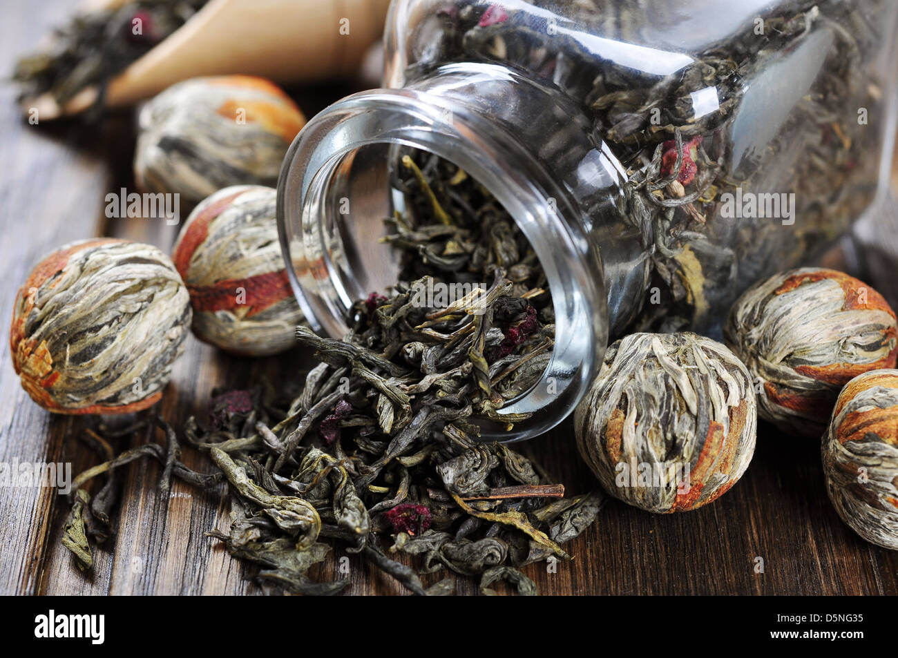 Grüner Tee-Kugeln mit Blumen und Glas mit Tee auf Holztisch Stockfoto