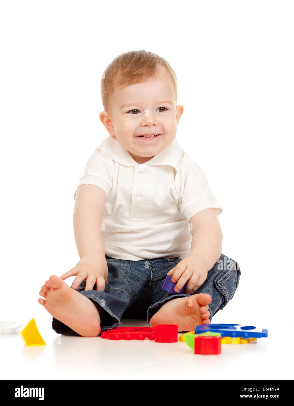 Nettes kleines Kind spielt mit Spielzeug beim Sitzen am Boden, isoliert auf weiß Stockfoto