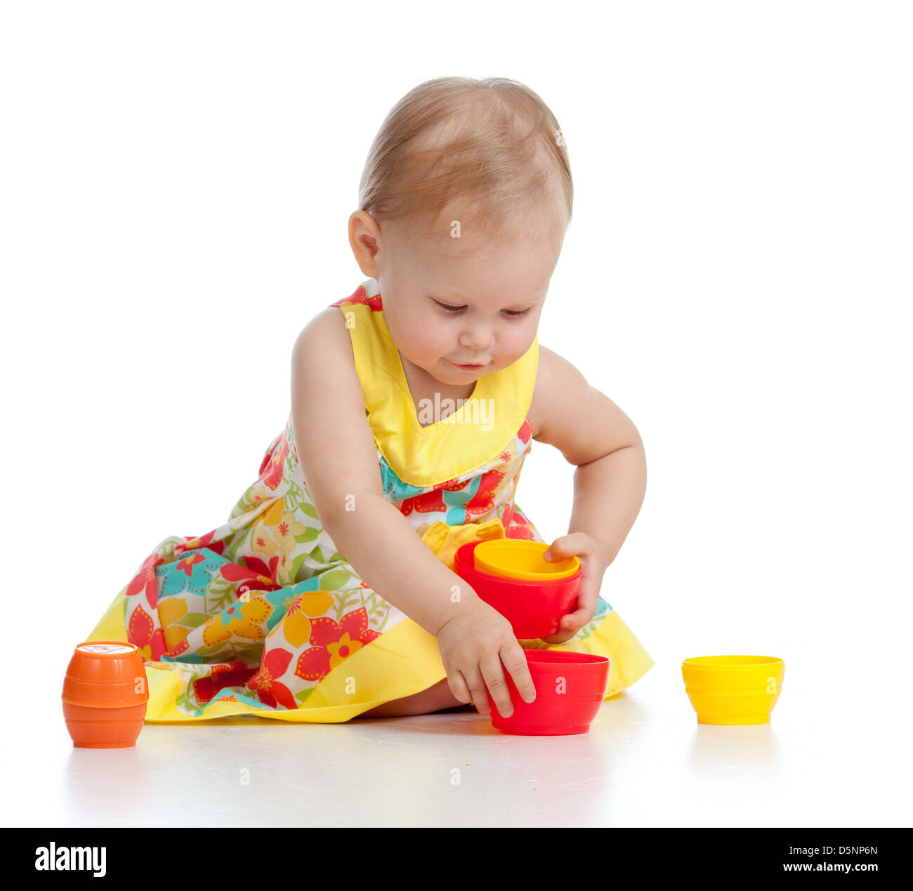 Nettes kleines Kind spielt mit Spielzeug beim Sitzen am Boden, isoliert auf weiß Stockfoto