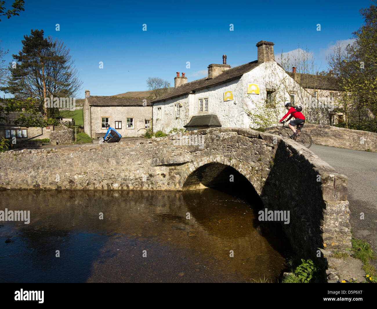 Großbritannien, England, Yorkshire, Malham, Radfahrer kreuzen alte Steinbrücke über den Fluss Aire Stockfoto