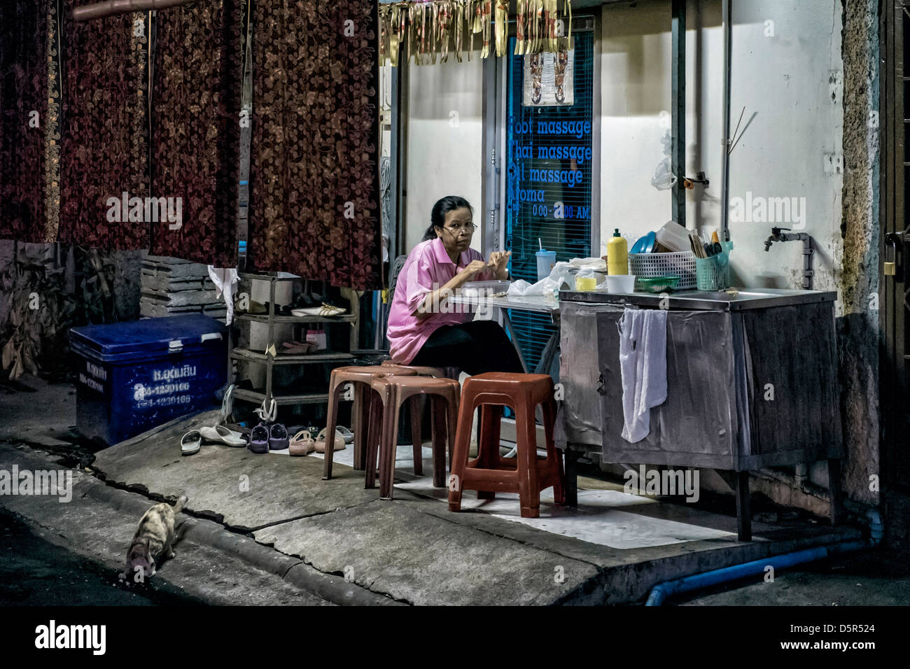 Bangkok-Seitenstraße-Szene von einer einsamen Frau und ihrer Katze essen in der Nacht. Thailand in Südostasien. Stockfoto