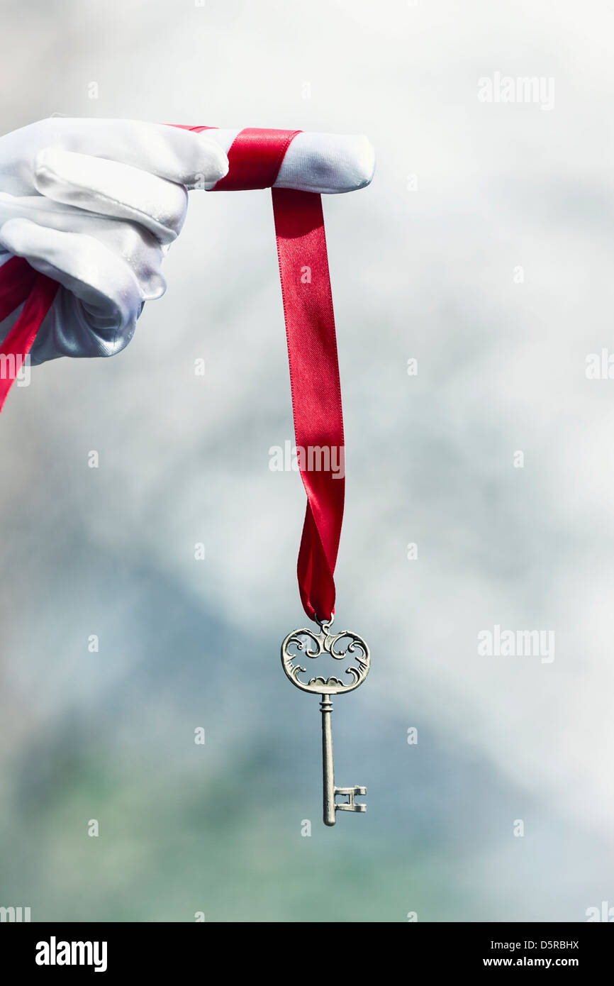 eine Hand in weißen Handschuhen hält einen alten Schlüssel auf einem roten Band Stockfoto