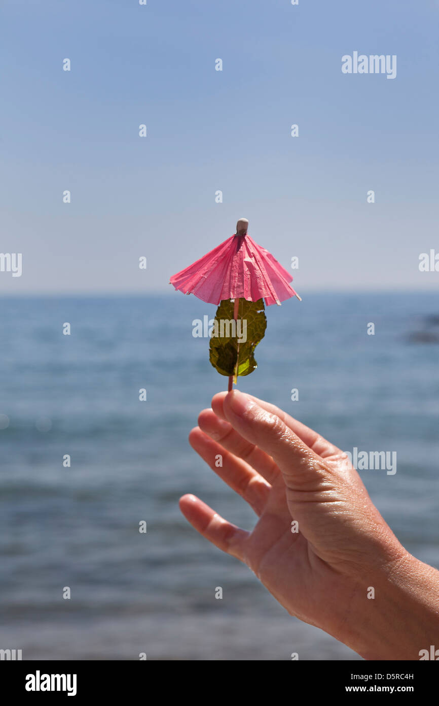 Eine Hand zeigt einen Regenschirm cocktail mit Minze am Strand in einem heißen sonnigen Tag Stockfoto