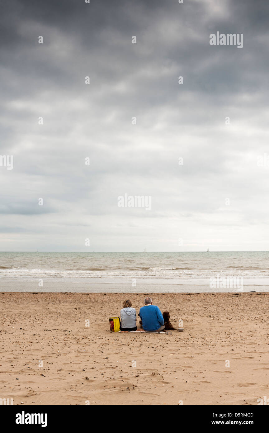 Ein Paar und ihr Hund am Strand zu sitzen bei Camber Sands, East Sussex, als Regen Wolken sammeln Stockfoto