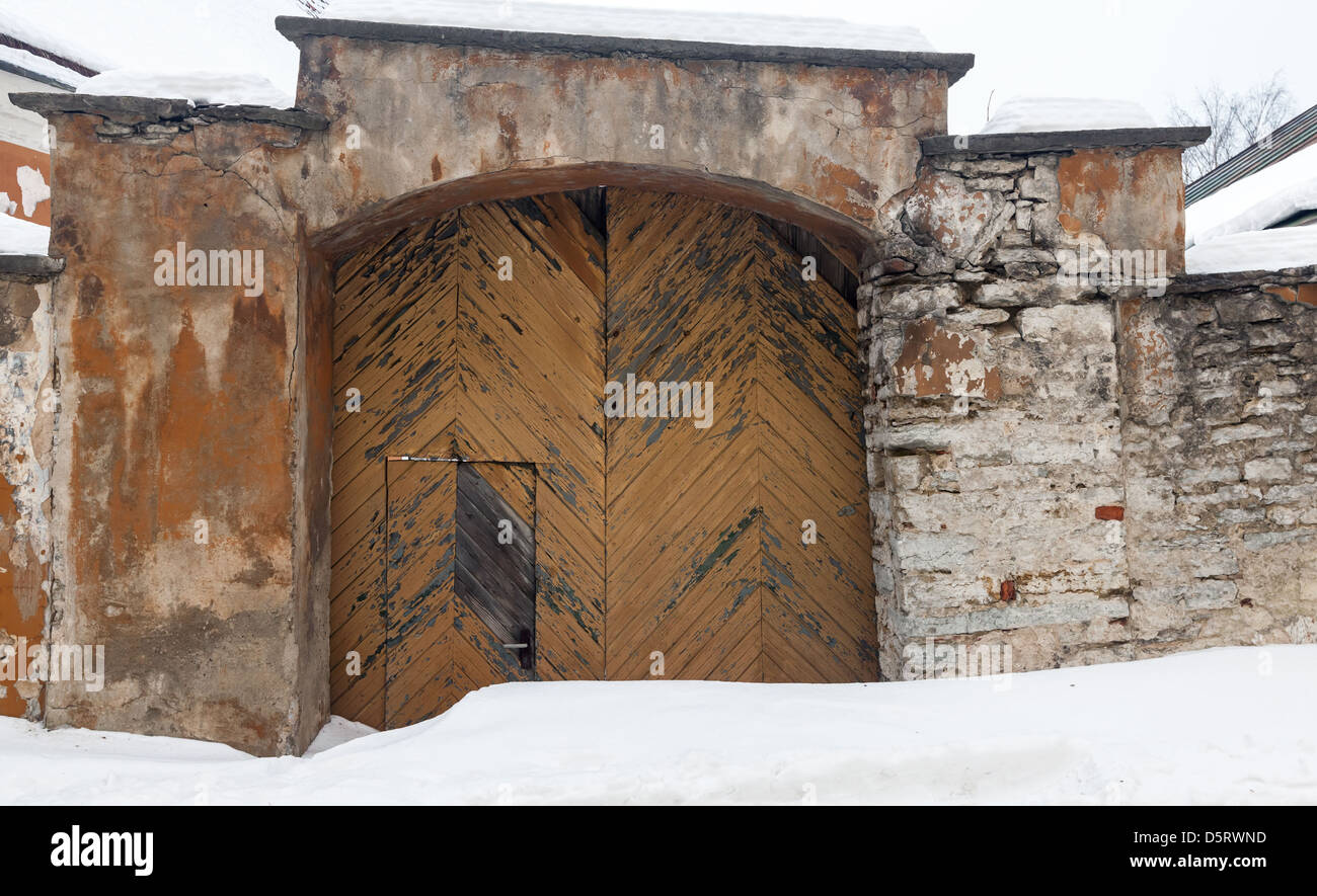 Steinmauer eines alten Gebäudes mit verwitterten Holztor und Schneewehe. Tallinn, Estland Stockfoto