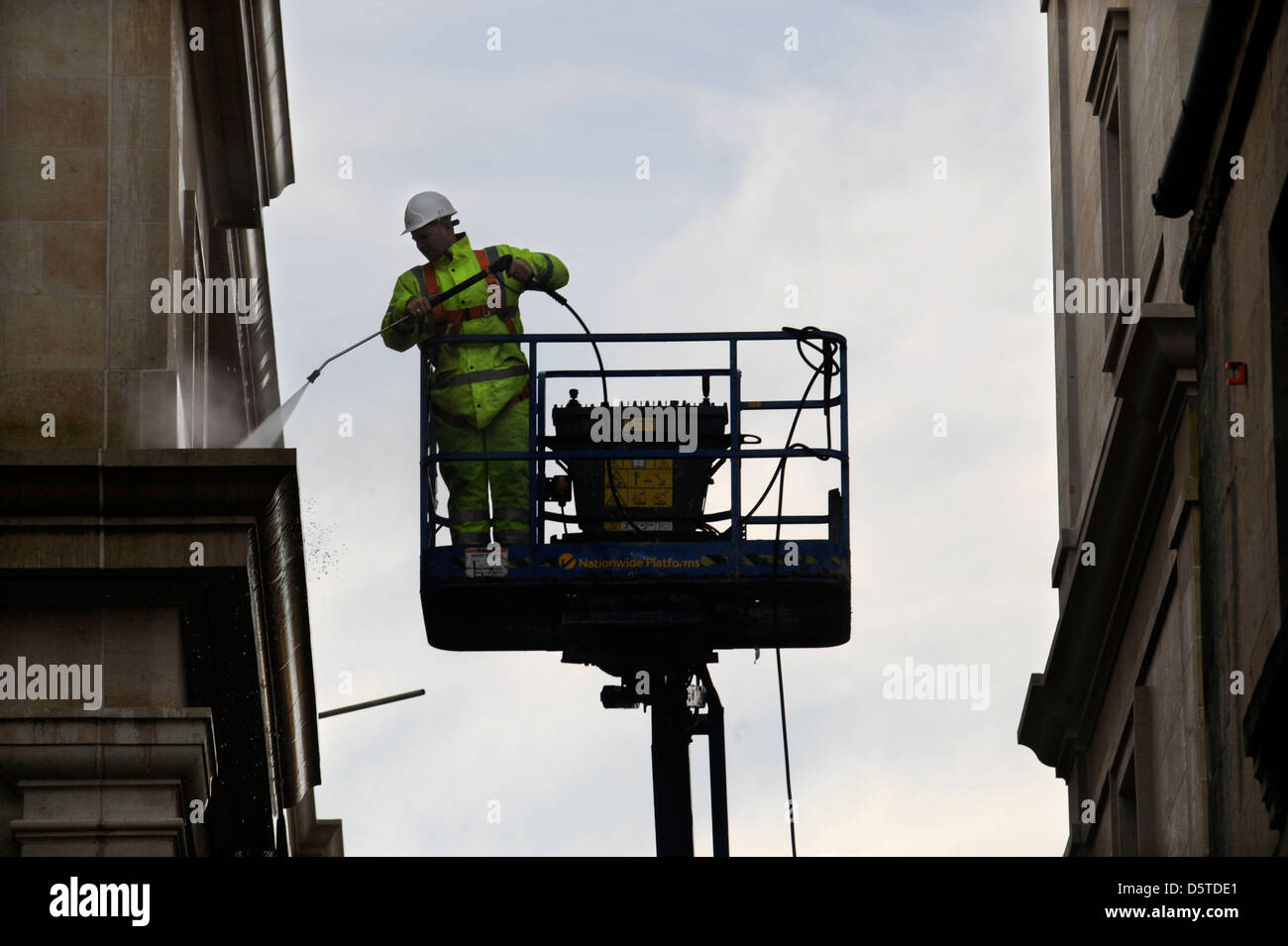 Ein Baumeister in eine Hubarbeitsbühne sprühen die Fassade des The Bad Southgate Einkaufszentrum Somerset UK Stockfoto