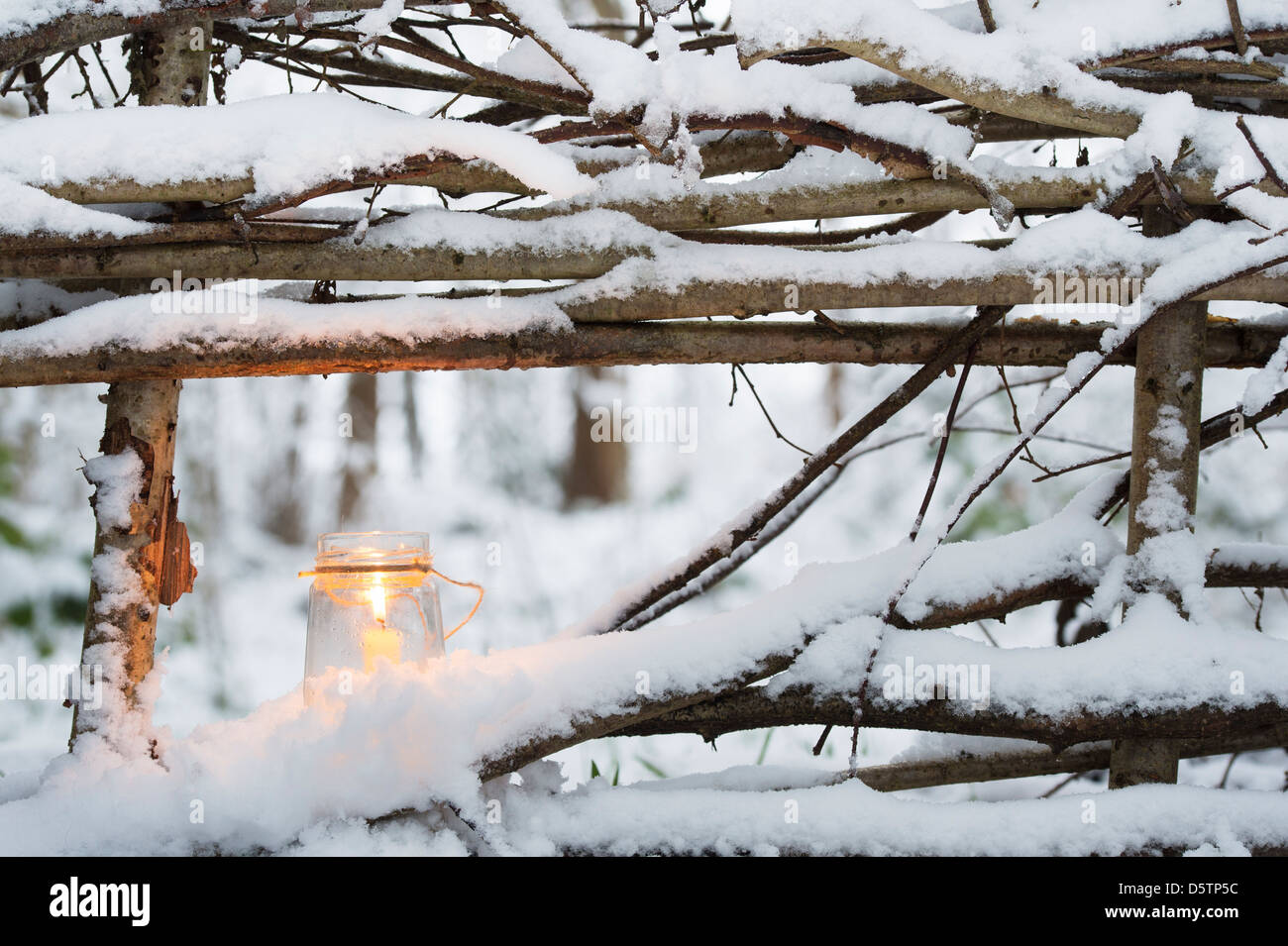 Weihnachtskerze in einem Glas auf einem natürlichen Zaun im Schnee bedeckt Holz Stockfoto