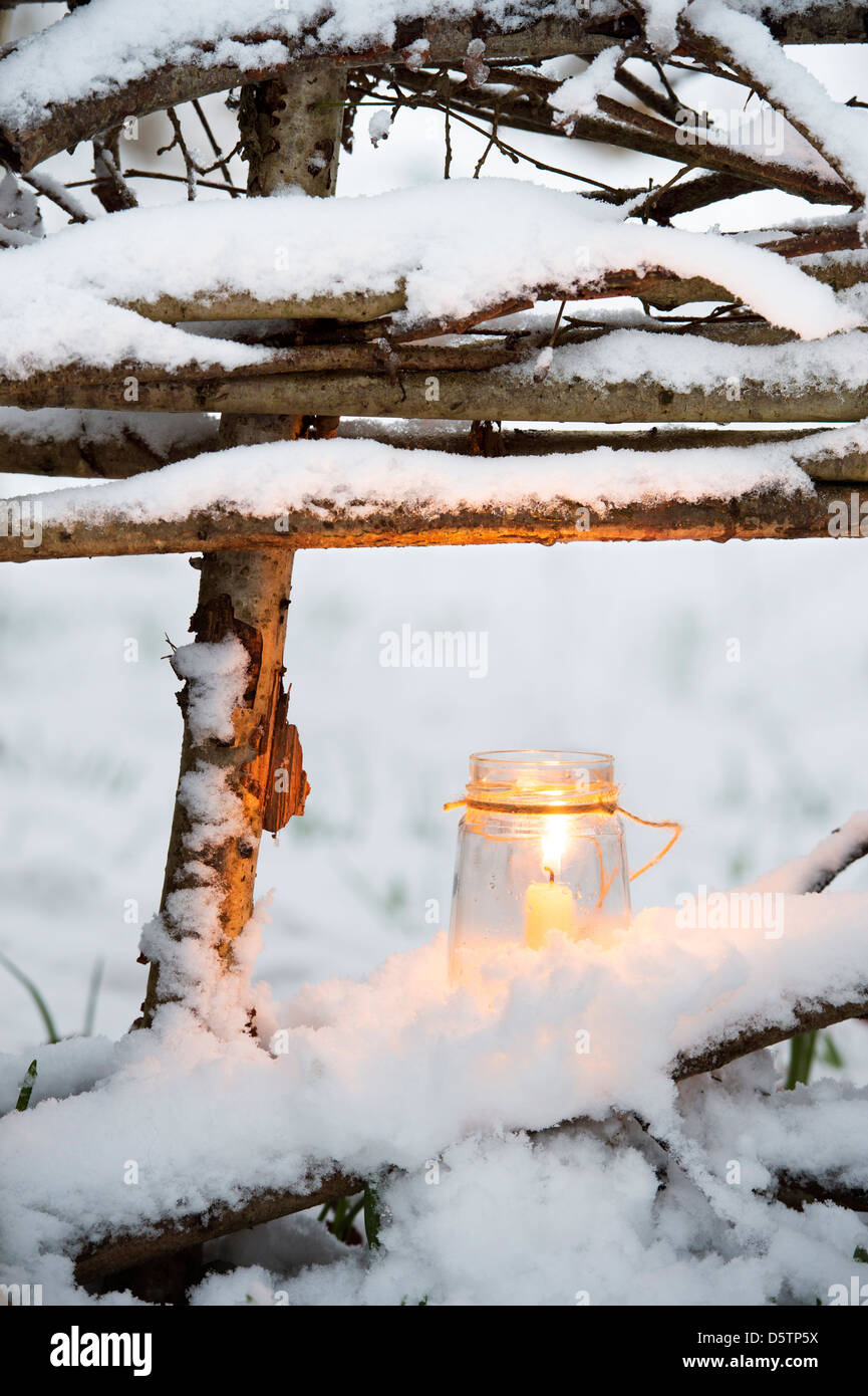 Weihnachtskerze in einem Glas auf einem natürlichen Zaun im Schnee bedeckt Holz Stockfoto