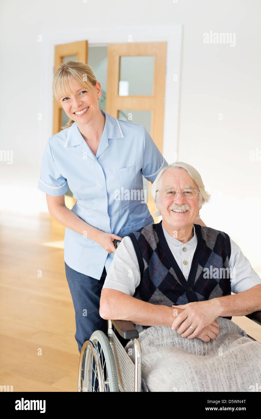 Pflegeperson älteren Mann im Rollstuhl schieben Stockfoto