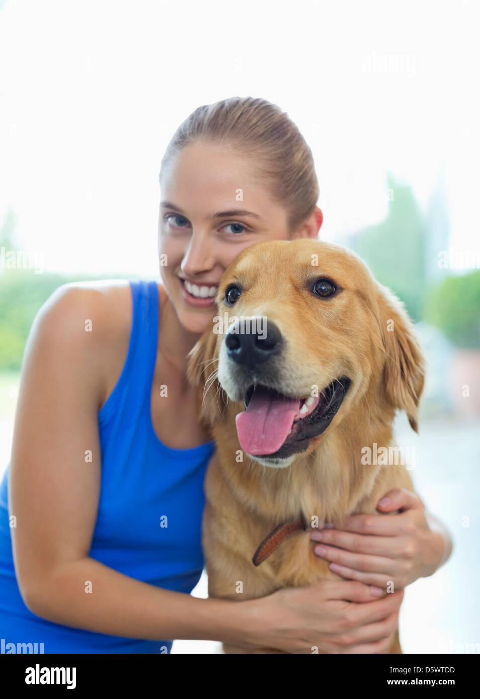 Lächelnde Frau umarmt Hund drinnen Stockfoto