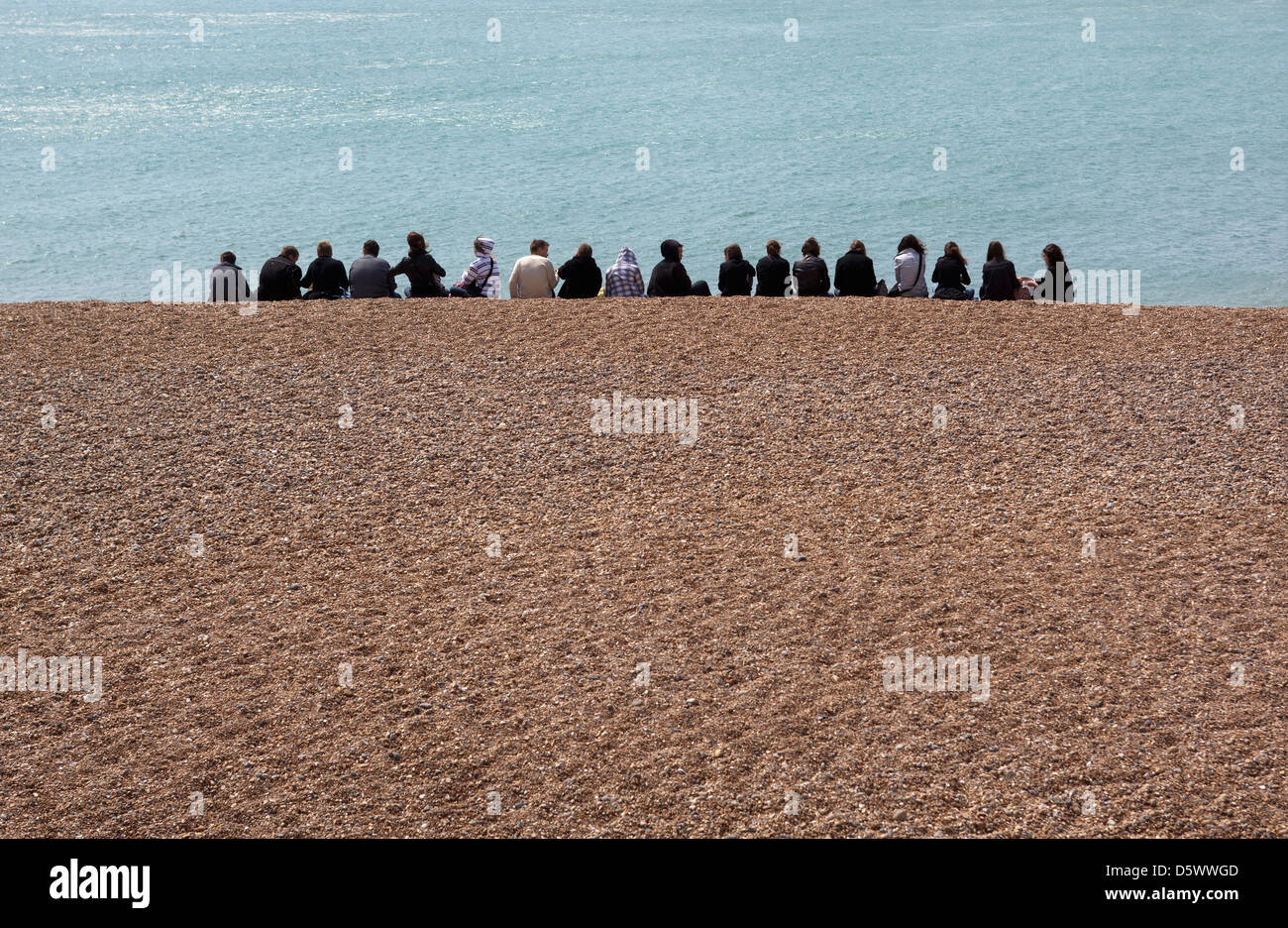 Gruppe junger Leute sitzen in Reihe am Strand von brighton Stockfoto