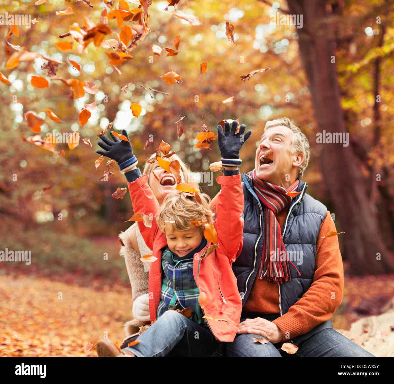 Älteres Ehepaar mit Enkel im Herbstlaub spielen Stockfoto