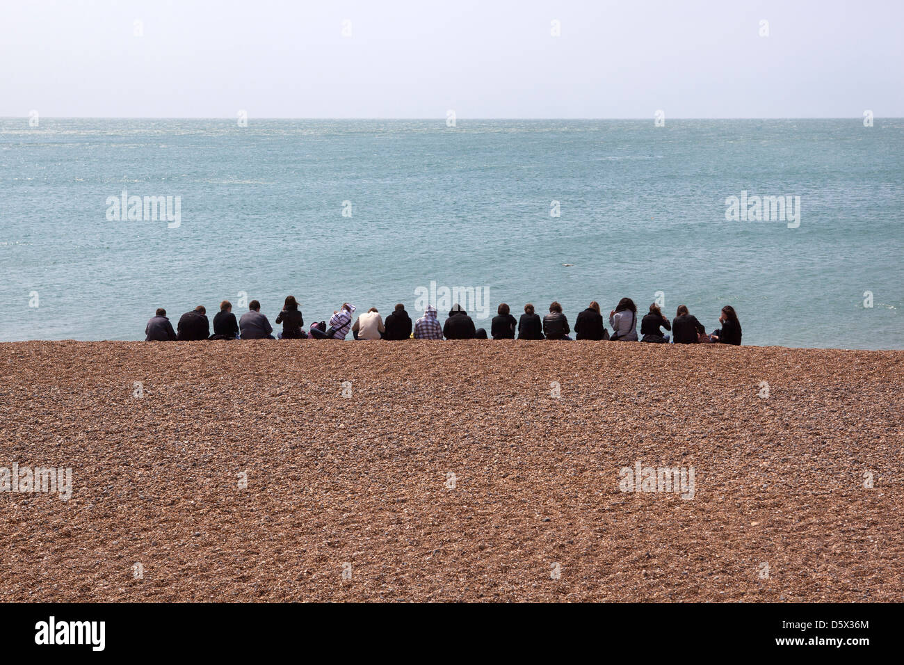 Gruppe junger Leute sitzen in Reihe am Strand von brighton Stockfoto