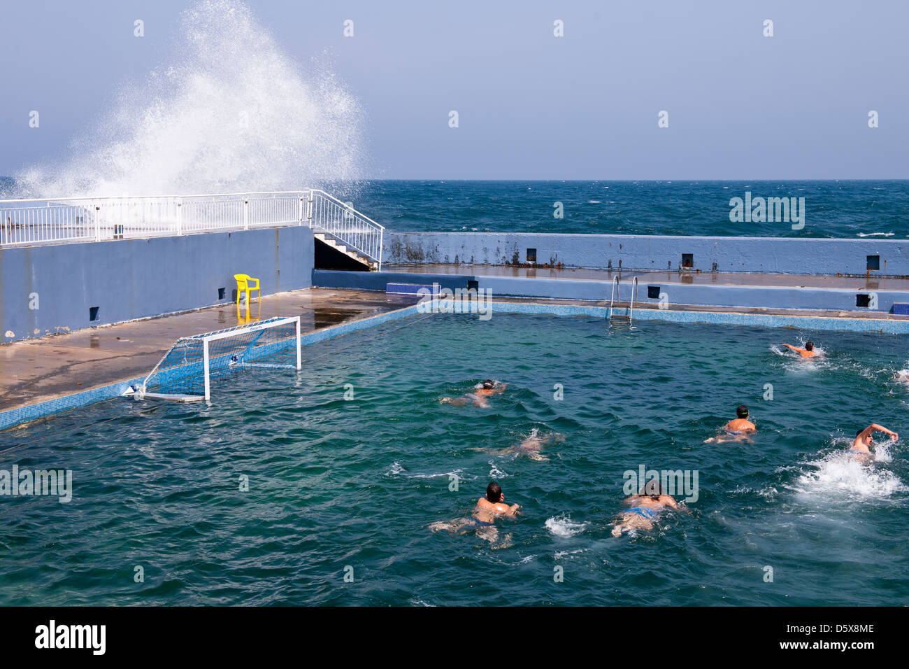 Schwimmer genießen die Sicherheit eines Pools, während die Wellen die Wand außen, Sliema, Malta zerschmettern Stockfoto