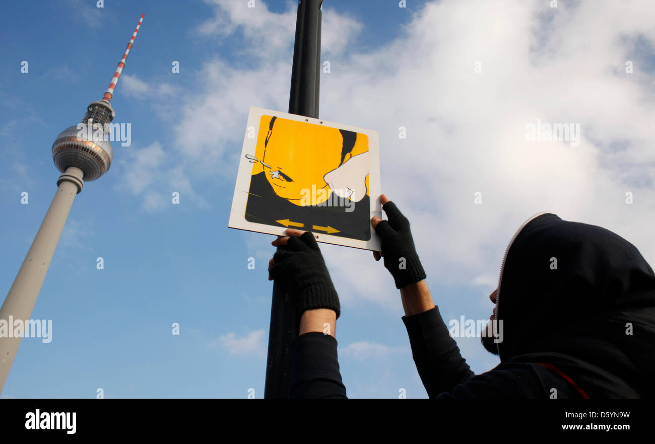 Künstler El Bocho zeigt, wie er eines seiner Piktogramme ein Wegweiser in Berlin, Deutschland, 31. Oktober 2012 beimisst. Das Bild zeigt eine Szene, in der jemand geschlagen ist, während jemand die Szene mit dem Handy filmt. Strett Künstler El Bocho aus Berlin begann eine Kunstaktion auf Gewalt in den großen Städten am 31. Oktober 2012. Er beabsichtigt, mehr als 250 Piktogramme Aufmachungen Stockfoto