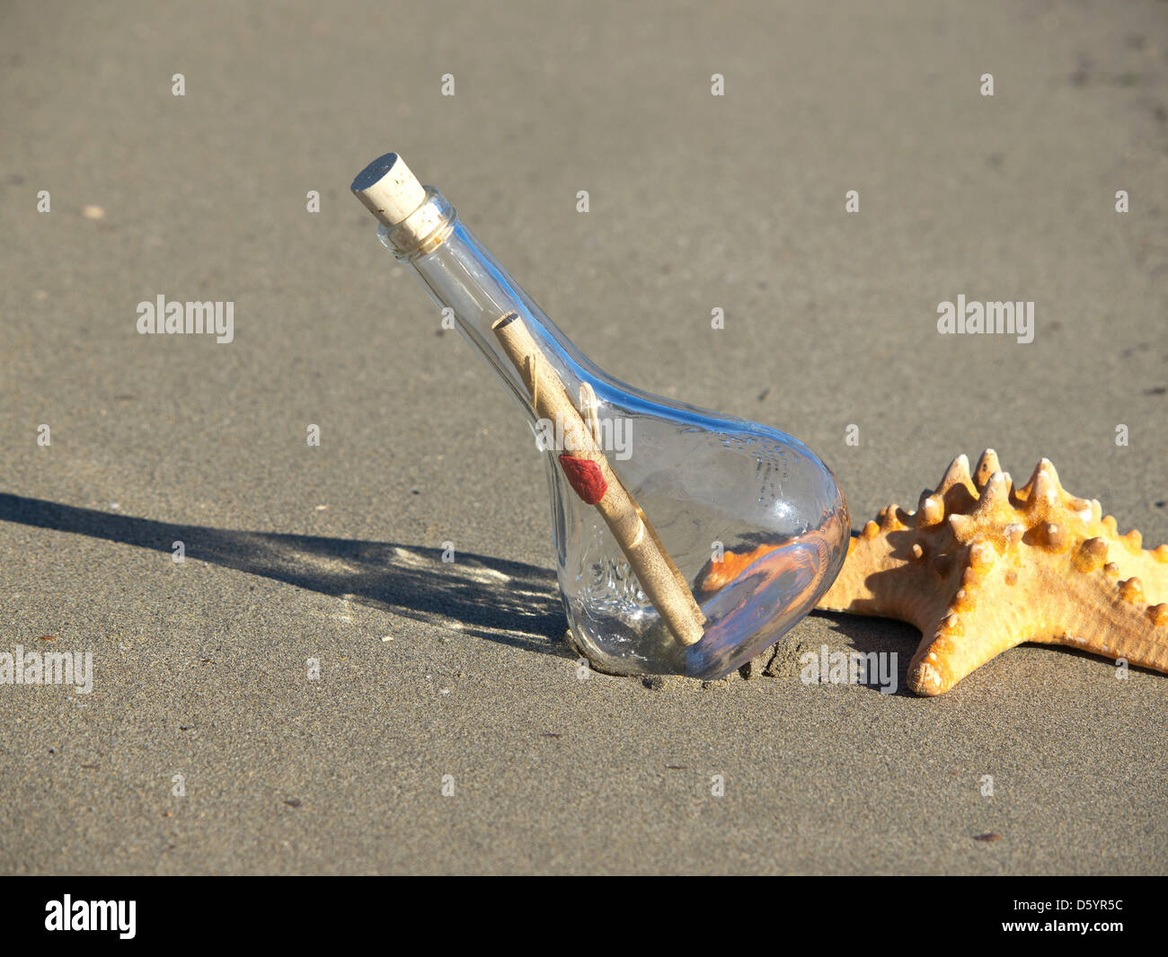 Nachricht in der Flasche und Seesterne am Sandstrand Stockfoto