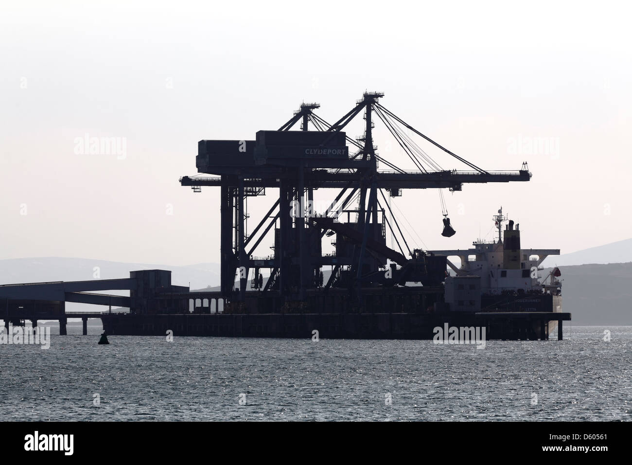 Silhouette von Kränen, die die Ladung eines Schiffes am ehemaligen Hunterston Coal Terminal am Firth of Clyde, Fairlie, North Ayrshire, Schottland, Großbritannien, entladen Stockfoto