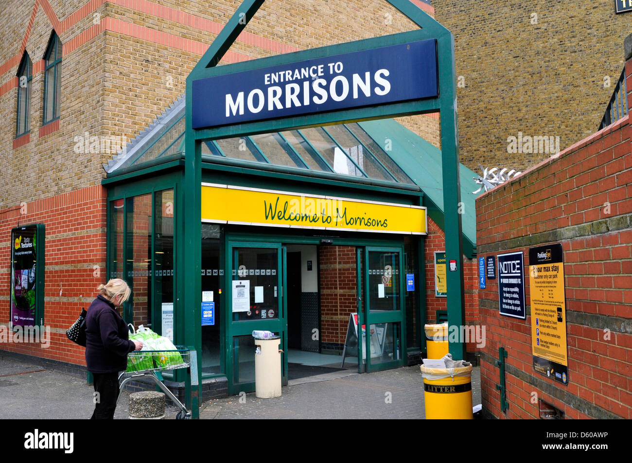 Eine Frau mit einem Einkaufswagen wartet außerhalb Morrisons Store in Acton, London, UK Stockfoto