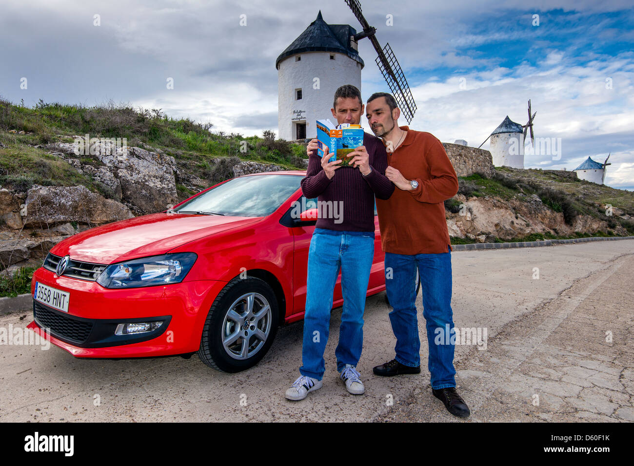 Kaukasische schwules Paar ein Buch touristische Führer mit typisch spanischen Windmühlen hinter in Consuegra, Kastilien-La Mancha, Spanien Stockfoto