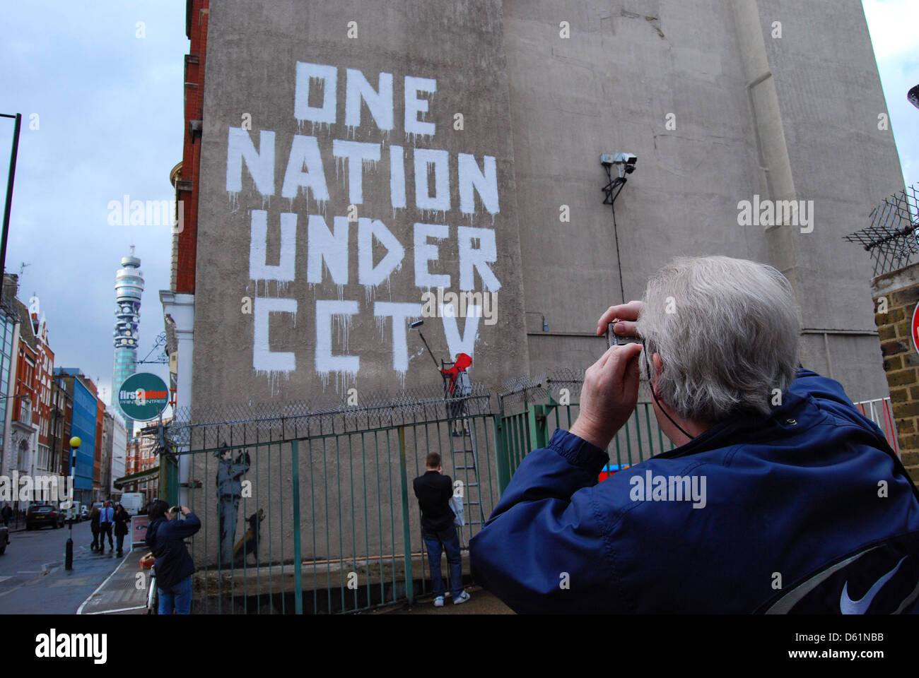 Eine Seniorin nimmt Fotos von Banksy Kunst in Newman Street, London, UK. Stockfoto